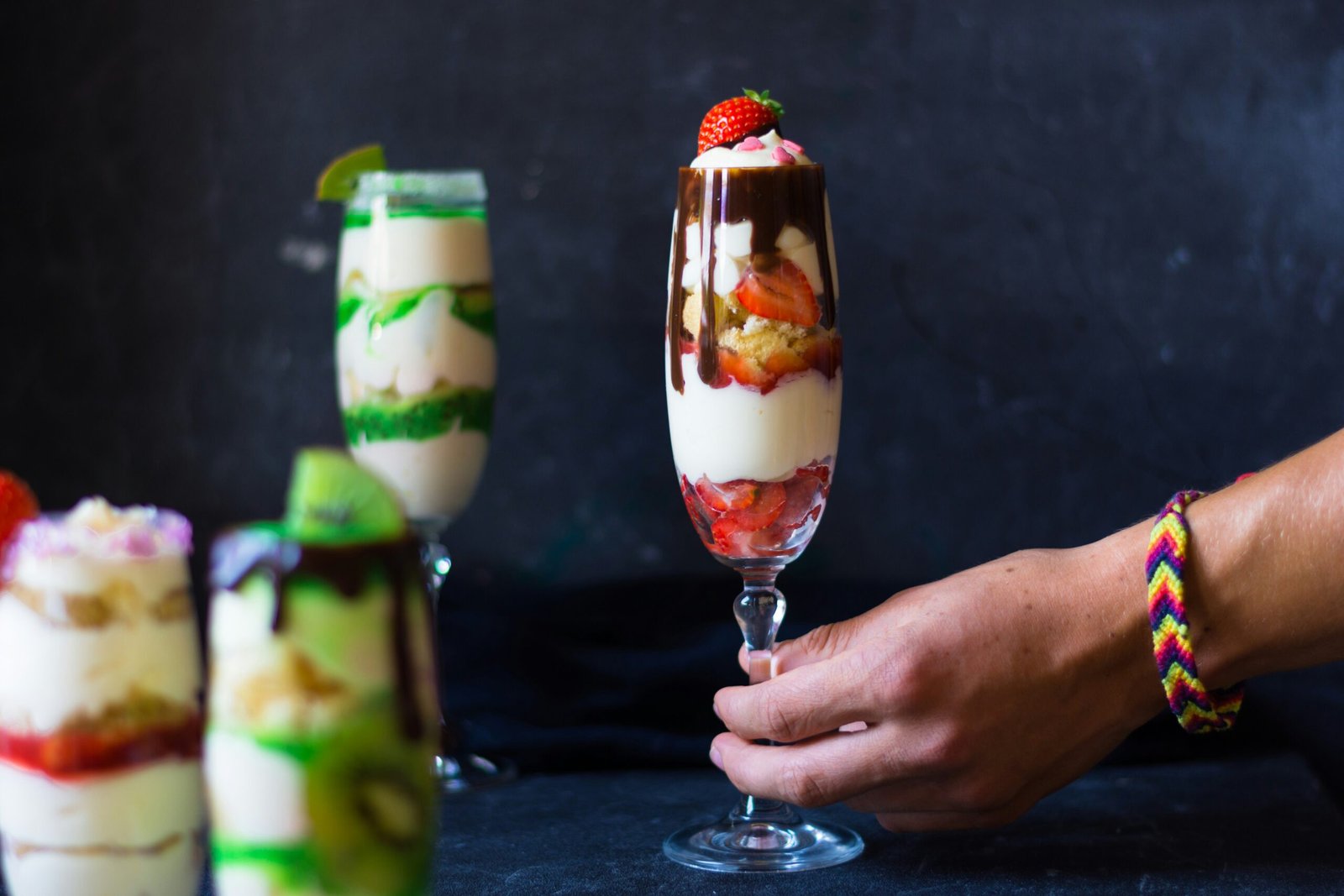 person holding clear glass footed cup with strawberry and cream